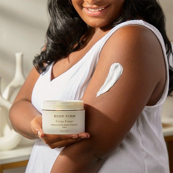 Woman with cream on arm holding Body Firm Advanced Body Care Treatment from Crepe Erase